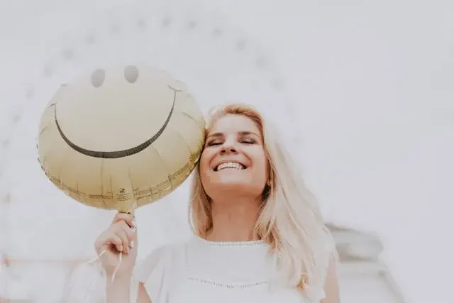 happy-woman-smiling-with-balloon Smiling woman holding a happy face balloon on a bright day.