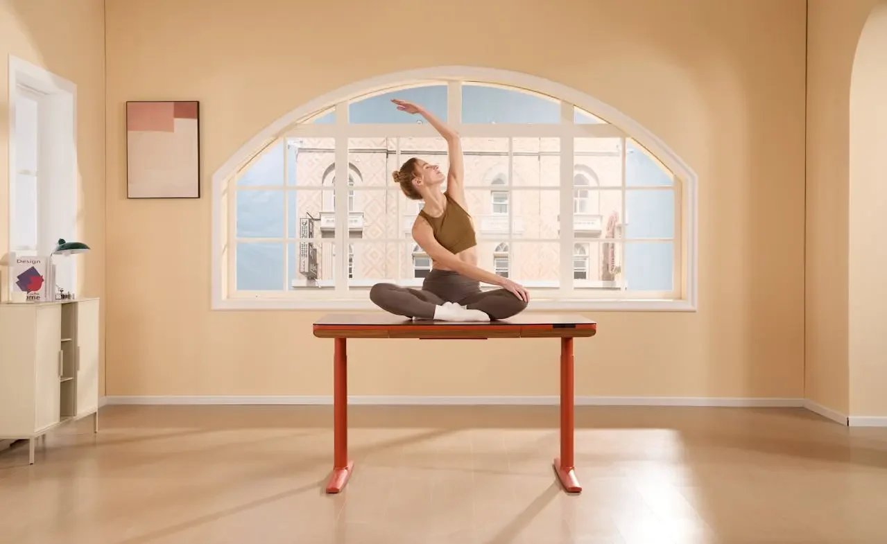 Woman practicing a seated side stretch on a desk in a minimalist, sunlit room with arched windows and warm tones.
