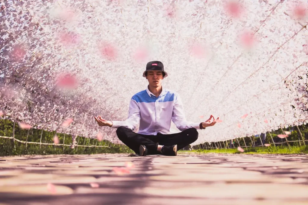 Young man meditating peacefully under a tunnel of pink cherry blossom petals, surrounded by soft light and spring atmosphere.