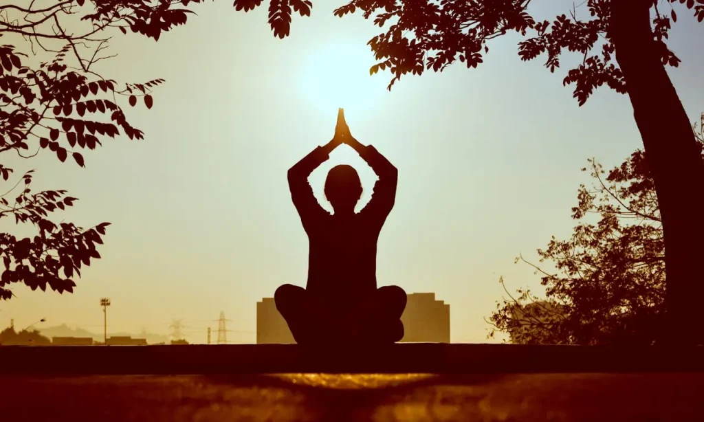 Person meditating outdoors at sunrise in a peaceful seated pose under trees